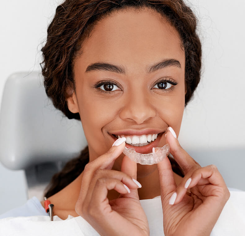 woman inserting a clear aligner onto her teeth